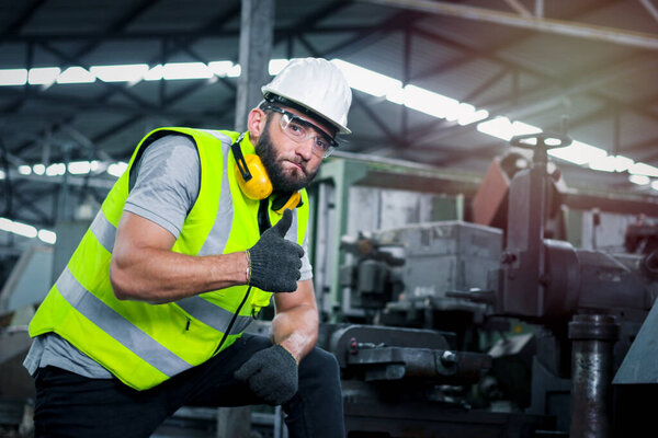 Портрет инженера-технолога в шлеме и защитных очках, стоящего и показывающего большой палец на заводе по производству