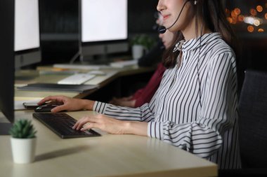 Klavyede el yazısı yazmak, kulaklıklı Asyalı bir kadın çağrı merkezindeki servis masasında gece arkadaşlarıyla çalışıyor, müşteriyle sohbet etmeye ya da sohbet etmeye hazır, mutlu iş yeri konsepti.