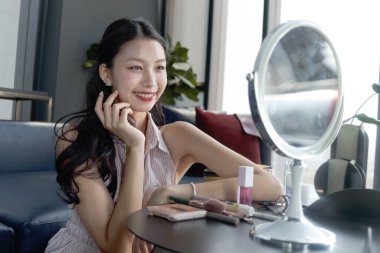 Female teenager looks at her beautiful appearance in mirror after applying makeup cosmetic on face at home. Happy teen Asian girl checking her appearance after finishing makeup. Beauty makeup cosmetic