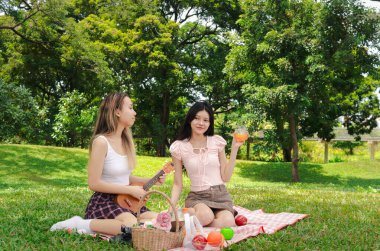 İki güzel Asyalı kadın yeşil parkta piknik yapıyor. Rahatlayan yakın arkadaş kızlar ukulele çalar, şarkı söyler ve dışarıda portakal suyu içerler. İnsanlar birlikte zaman geçirir. Doğa ile iç içe..