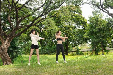 Spor giyimli iki Asyalı kadın doğa yeşil parkında vücut esnetiyorlar. Spor kankası kızlar yeşil bahçede spor yapar. Sportif kız, doğada partnerle sağlıklı egzersiz yapar..
