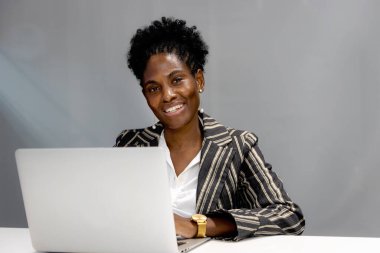 Ofiste bilgisayarla çalışan kıvırcık saçlı, gülümseyen Afrikalı iş kadınının portresi. İş yerinde çalışan güzel bir kadın işçi. İş yerindeki mutlu iş adamları.