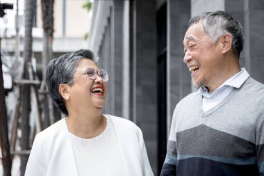 Mutlu üst düzey Asyalı çift birbirlerine bakıp bina dışında birlikte gülüyorlar. Şehrin girişinde duran olgun, yaşlı aşıklar gibi gülümsüyorsun. Emekli insanlar birlikte dışarıda vakit geçiriyorlar..