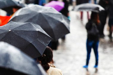 Yağmurlu havada şemsiyeli bir sürü insan. Yüzü yok. Arkadan manzara..