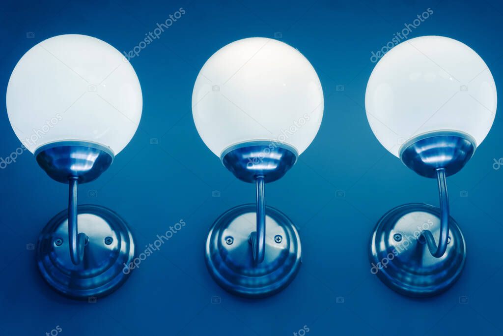 Round wall lights. Three bright lamps against a blue wall. Close-up