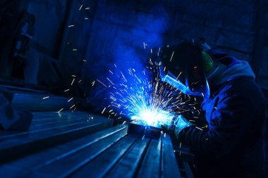 Kaynakçı metal bir profil üzerinde çalışıyor. Endüstriyel üretimde metal yapıların birleştirilmesi
