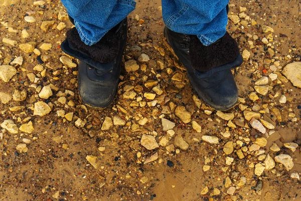 Legs of a tourist in big boots on the river bank. View from above. Close-up