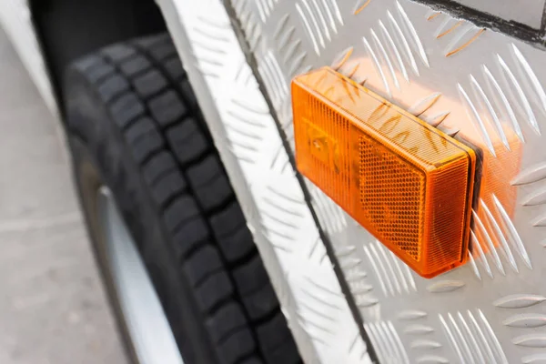 Turn signal on the truck. Fragment of a truck with an orange turning signal on the background of the wheel.