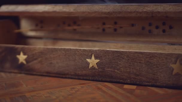 L'encens (bâtonnets d'encens) fume dans une boîte en bois unique avec une étoile. Doucement. La fumée sort des trous. La boîte est sur une table faite à la main. Gros plan. Dans le sens inverse des aiguilles d'une montre. Focus sur la fumée et l'encens.