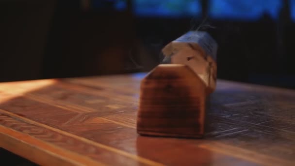 星付きのユニークな木箱から香 煙が穴から出てくる 箱は手作りのテーブルの上にある 接近中だ 反時計回りの回転 青い窓のある黒の背景 — ストック動画