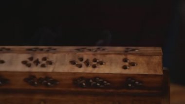 Duman eşsiz bir ahşap tütsü kutusundan (tütsü çubukları) çıkar. Saat yönünün tersine dairesel hareket döngüsü. Yakın plan. Dumana odaklan. Siyah arkaplan.
