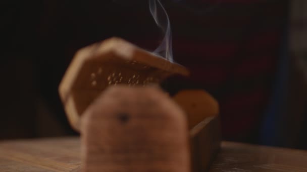 La fumée sort d'une boîte d'encens en bois unique (bâtonnets d'encens). La fumée sort des trous de la boîte. Boîte sur une table faite à la main. Gros plan. Concentre-toi sur la fumée. Fond noir.