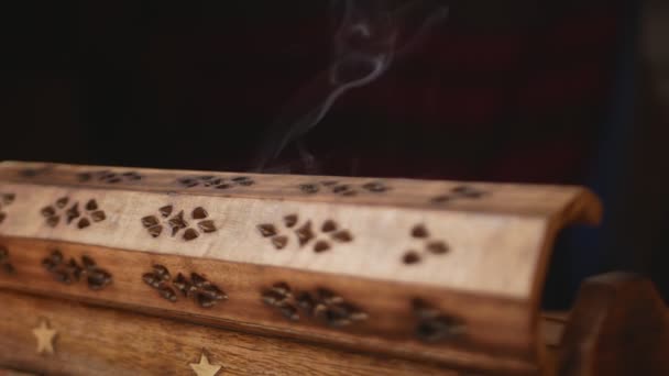 La fumée coule de l'encens (bâtonnets d'arôme) dans une boîte en bois unique. Cycle.Smoke sort des trous de la boîte. Boîte sur une table faite à la main. Gros plan. Mouvement d'un côté à l'autre.Concentrez-vous sur la fumée. Fond noir.