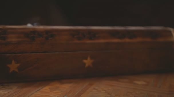 La fumée sort d'une boîte d'encens en bois unique (bâtonnets d'encens). La fumée sort des trous de la boîte. Boîte sur une table faite à la main. Gros plan. Rotation rapide dans le sens inverse des aiguilles d'une montre. Fond noir.Cycle.