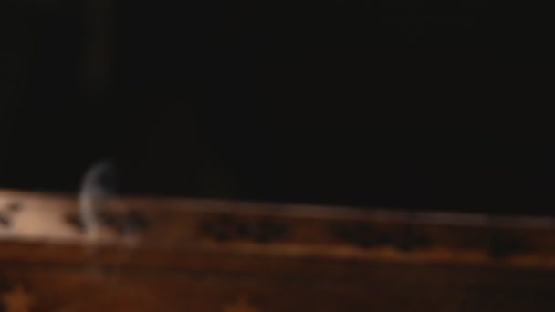 Des couches de fumée s'écoulent d'une boîte d'encens en bois unique qui tourne. La fumée sort des boîtes avec des trous, la boîte est floue. Concentre toi sur la fumée. Fond noir.