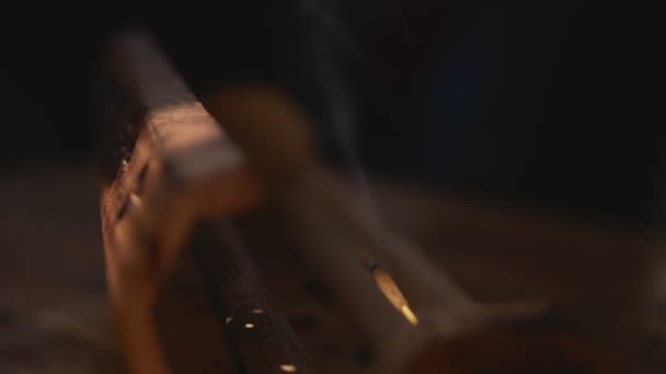 Bâton d'encens est fumé à partir d'une boîte en bois unique ouverte, demi-tour cyclique. La boîte sort dans la lumière et va dans les ténèbres. Mettez l'accent sur le bien-être et la fumée. Fond noir.