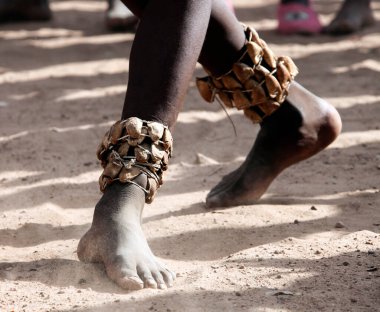 Kum ayini dansında dans eden siyah bir gencin ayakları. Kum ve tozda ayak bileği süslenmiş siyah bir Afrikalı 'nın sağ bacağı..