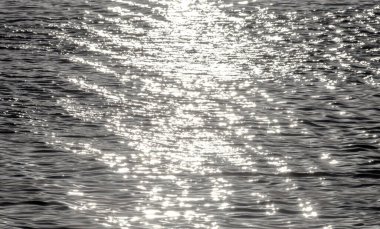 Su yüzeyinin arka planında dalgalar, dalgalar ve güneş ışığı var. Güneşin dokusu, gölün çevresindeki ışığın tatlı sularında iz bırakır..