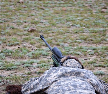 Teleskopik görüşlü bir tüfekle ateş etmeden önce kamuflajlı bir tetikçi. Keskin nişancı uzun menzilli görüş sistemi kullanarak doğru atış için hazırlanıyor..
