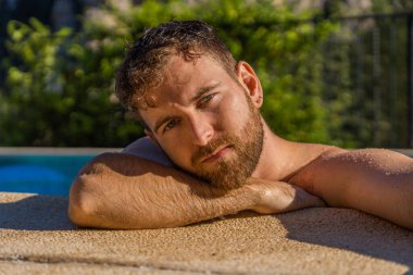 Sarışın, kısa sakallı, yeşil ve mavi gözlü bir çocuğun portresi. Arka planda dağlar ve yüzünde sıcak güneş ışığı olan bir havuzda kuzey özellikleri var.