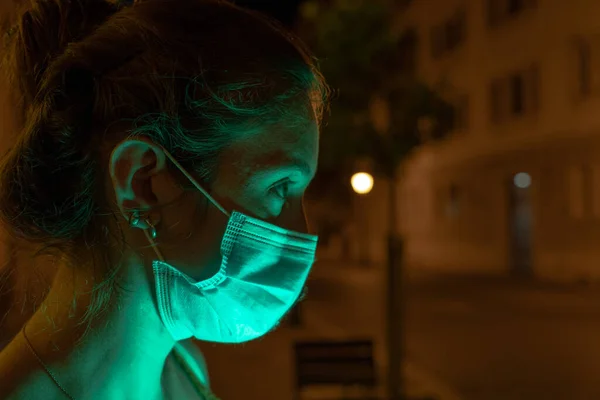 在街上 年轻的西班牙女人在夜间使用手机 脸上带着面具 对着科维德 街上没有人作为背景 脸上闪烁着光芒 — 图库照片