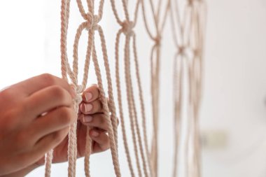 Kadın ellerinin yakın plan çekimleri bej ipli makrome perdeler ve parlak ışıklı beyaz arka plan