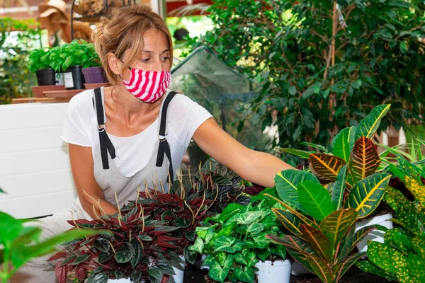 woman with mask works in a plant nursery - woman with mask with a flower pot in her hand