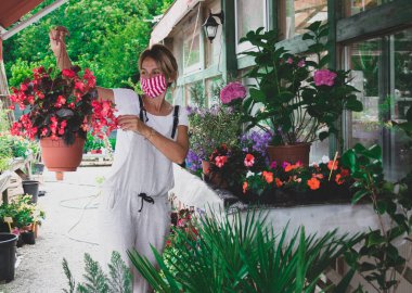 Çiçek saksısı elinde ve yüzünde maskeyle bir fabrikada çalışan bir işçi.