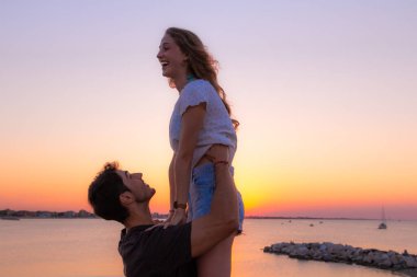 Gün batımında eğlenen genç aşıklar. Bir adam gün batımında kız arkadaşına sarılıyor. Aşk ve eğlence konsepti.