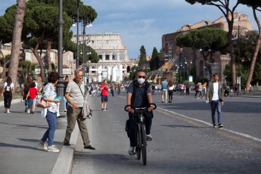 ROME, ITALY - Haziran 02 2020: İtalya yeniden açılıyor, 3. aşama başlıyor koruyucu maske takan bisikletçi Roma, İtalya 'da Colosseum (Colosseo) yakınlarındaki Fori Imperiali caddesinde yürüyor