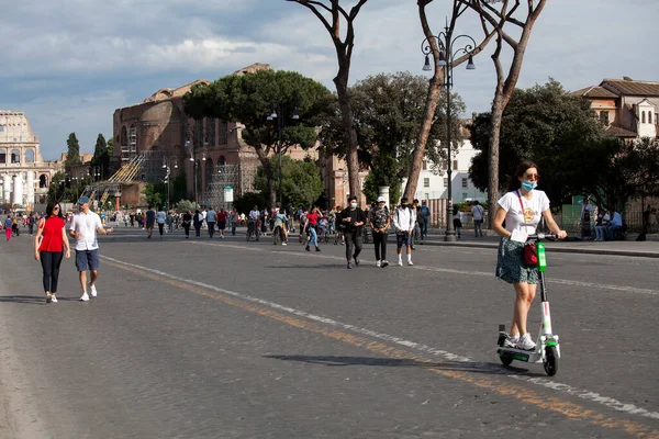ROME, ITALY - Haziran 02 2020: Koruyucu yüz maskesi takan kadın, İtalya 'nın orta kesimindeki Piazza Venezia yakınlarındaki Via dei Fori Imperiali' ye gitmek için elektrikli scooter kullanıyor. Limonlu scooter.