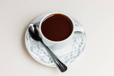 Beyaz bir fincan, bir kaşık ve bir peçete üzerinde küçük beyaz bir fincan koyu sıcak çikolata.