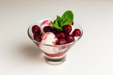 Donmuş kirazlı vanilyalı dondurma, naneyle süslenmiş, şeffaf bir kasede servis ediliyor.