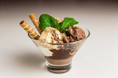Çikolata ve vanilyalı dondurma, fındık ve çikolata şurubuyla kaplı, çikolatalı waffle ve nane ile süslenmiş, şeffaf cam bir kasede servis ediliyor.