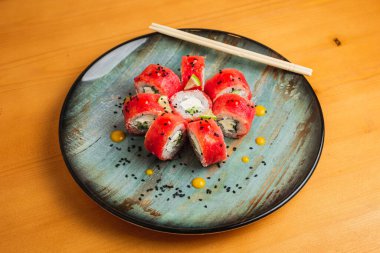 Avokado, krem peynir ve siyah sesam tohumlu ton balıklı rulo, mavi tabakta servis edilir.