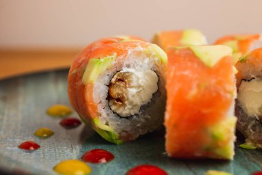 Avokado ve Philadelphia peynirli taze somon ve yılan balığı rulosu, mavi tabakta servis edilir.