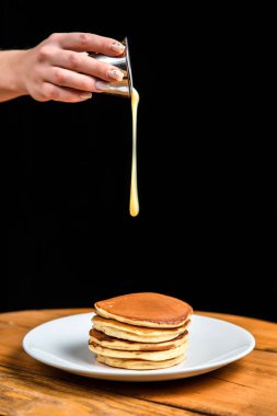 Beyaz bir tabakta bir yığın krep ve üzerine yoğunlaştırılmış süt döken bir el.