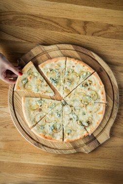 Bir kadının eli ahşap bir tahtadan bir dilim pizza çalıyor.