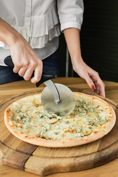 Cutting pizza with a pizza cutter, served on a wooden round board, natural light