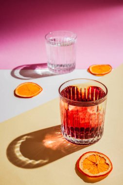 Kırmızı şuruplu iki buzlu bardağın çok parlak dikey fotoğrafı sert gölgeli sert ışık, turuncu cips. Pembe, beyaz ve sarı arkaplan