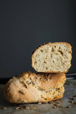 Ekmeğin yarısı kesilmiş, yarısı birbiri üzerine kesilmiş, ayçiçeği tohumlarıyla kaplı, kabartma kağıdında, dikey fotoğrafta.
