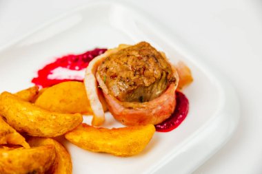 Fileminyon domuz pastırmasında sarılmış ve fırında böğürtlen sosuyla pişirilmiş. Garnitür için patates. Yakın plan fotoğraf.