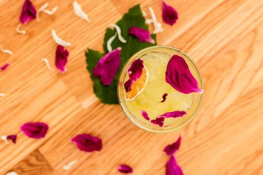 Kuru portakal dilimi ve gül yapraklarıyla süslenmiş buzlu ferahlatıcı narenciye kokteyli.