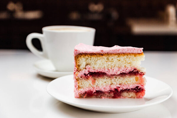 Strawberry yoghurt cake on a white plate and a cup of cappuccino coffee