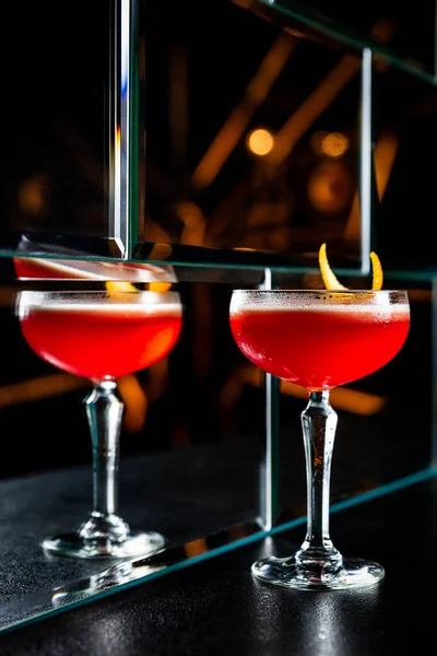 Röd Sur Cocktail Ett Coupeglas Garnerat Med Apelsinskal Reflektion Glasvägg — Stockfoto