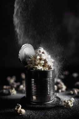 Çelik bir teneke kutuda tuzlu patlamış mısır, karamsar bir fotoğraf.