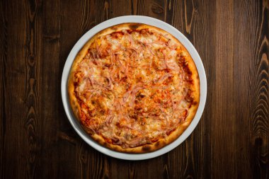 Jambon ve peynirli pizza, ahşap arka plan, sade bir üst görüş.