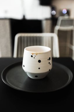 Üzerinde kahve damlaları olan beyaz bir fincan, siyah bir tabakta, siyah bir masada, bir kafede.