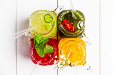 Kavanozlarda 4 farklı ferahlatıcı yaz limonatası, kırmızı, turuncu, sarı ve yeşil, üst manzara