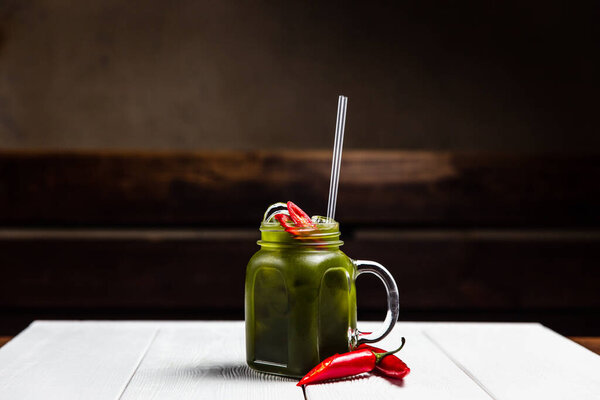 A refreshing summer lemonade with red chili pepper, in a jar, on white wooden table